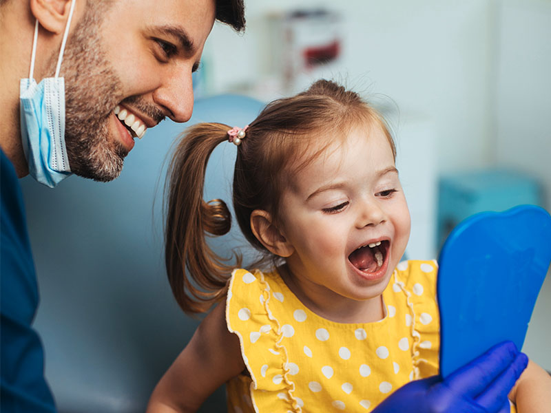 Dentist holding up mirror for toddler to look at their teeth.